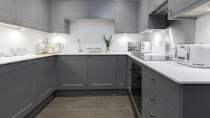 Una cocina moderna con armarios grises, encimeras blancas y electrodomésticos de acero inoxidable.