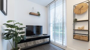 Una sala de estar moderna con un televisor de pantalla plana sobre una consola de madera, una planta grande en maceta y un reloj montado en la pared.