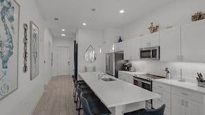 A modern kitchen with white cabinets, a stainless steel refrigerator, a microwave, and a long island with bar stools. - Newly Built Condo w/ 3 Pools & Steps to Beach + Free Attraction Tickets! (Santa Rosa Beach)