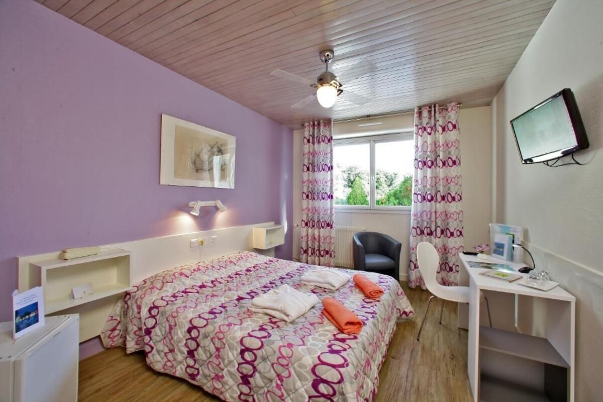 A bedroom with a bed, desk, chair, and a television.