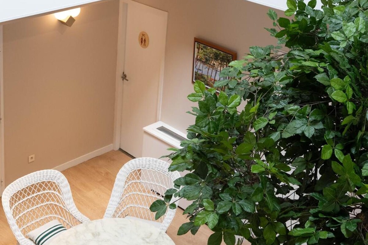 A small outdoor seating area with a round table and wicker chairs, a potted plant, and a door with a restroom symbol.