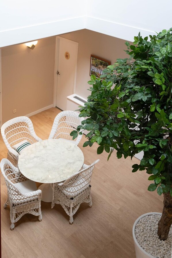 A small outdoor seating area with a round table and wicker chairs, a potted plant, and a door with a restroom symbol. - Logis Hotel Thermal (Saubusse)
