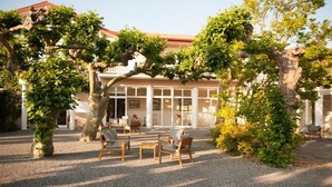 A building with a covered outdoor seating area, surrounded by trees and gravel. - Logis Hotel Thermal (Saubusse)