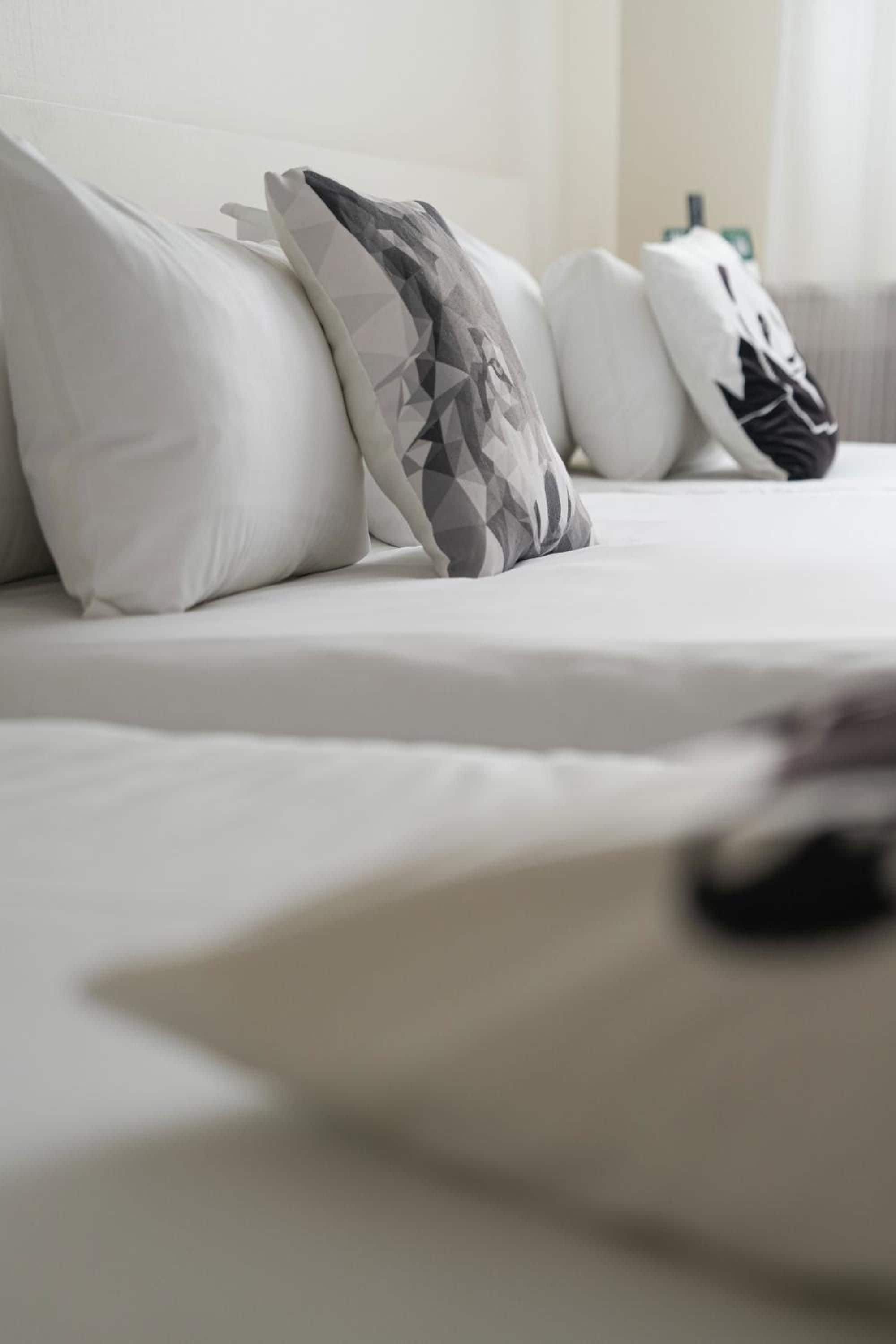 Un lit avec une literie blanche et un coussin à motifs géométriques.