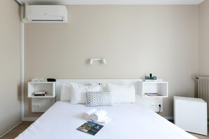 A hotel room with a bed, a bedside table, a nightstand, a wall-mounted heater, and a small radiator. - Logis Hotel Thermal (Saubusse)