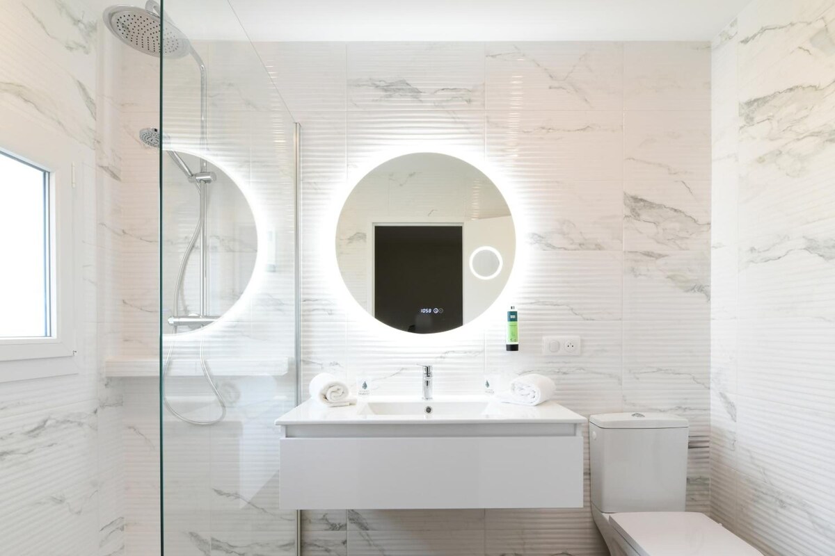 A modern bathroom with a glass-enclosed shower, a white sink with a mirror, and a toilet.