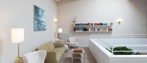 Un salon moderne comprenant un canapé, des fauteuils, une table basse, une bibliothèque et donnant sur un balcon.