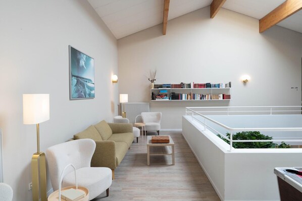 A modern living room with a sofa, chairs, a coffee table, a bookshelf, and a view of a balcony. - Logis Hotel Thermal (Saubusse)