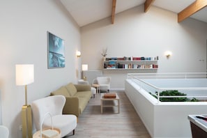 A modern living room with a sofa, chairs, a coffee table, a bookshelf, and a view of a balcony. - Logis Hotel Thermal (Saubusse)