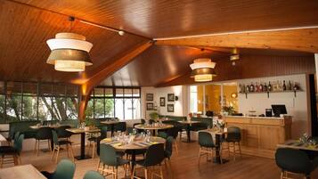 A restaurant with wooden ceiling beams, round tables, and green chairs.