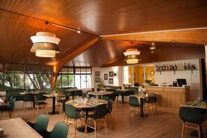 A restaurant with wooden ceiling beams, round tables, and green chairs. - Logis Hotel Thermal (Saubusse)