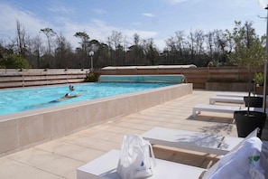 A swimming pool with a wooden deck, lounge chairs, and a bag labeled 'SAUBUSSE' on the ground. - Logis Hotel Thermal (Saubusse)