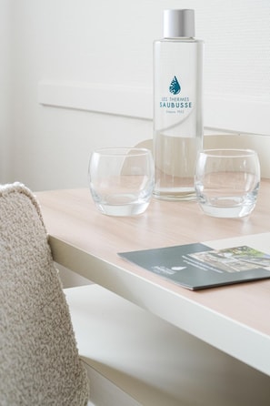 A clear glass bottle with a label, two clear glasses, and a brochure on a wooden surface. - Logis Hotel Thermal (Saubusse)