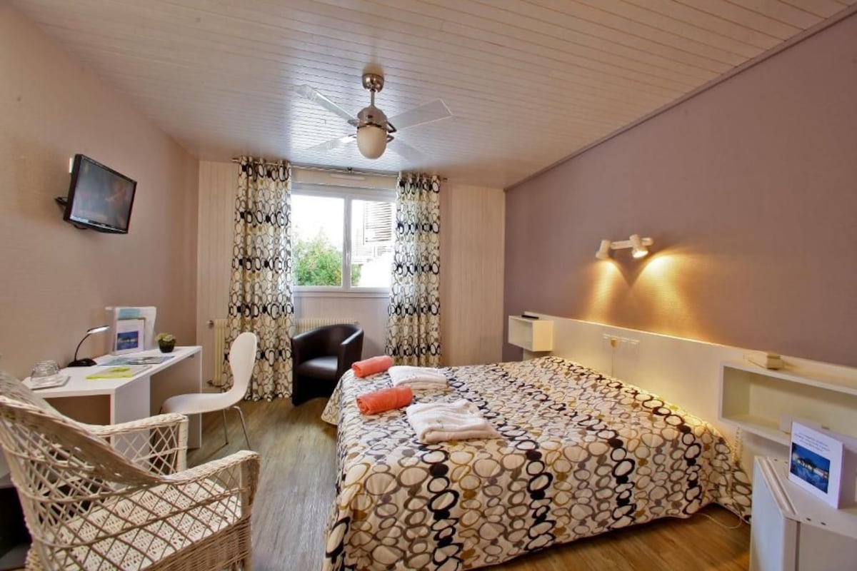 A bedroom with a bed, a desk, a chair, a television, and a window with curtains.