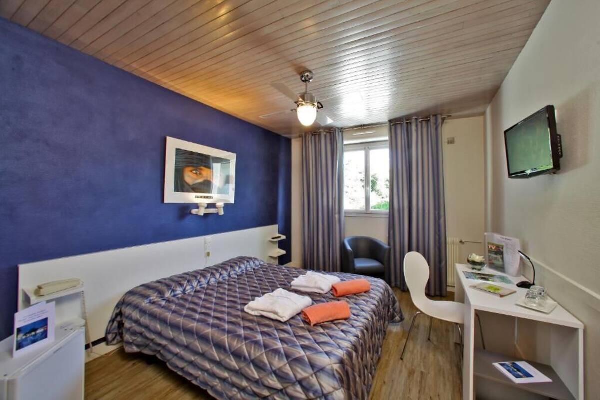 A hotel room with a bed, a desk, a chair, a television, and a window with curtains.
