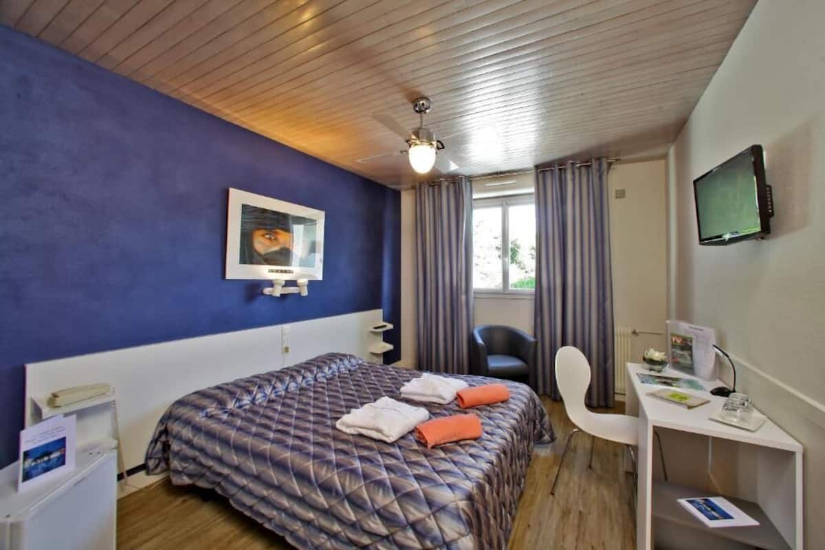 A hotel room with a bed, a desk, a chair, a television, and a window with curtains.