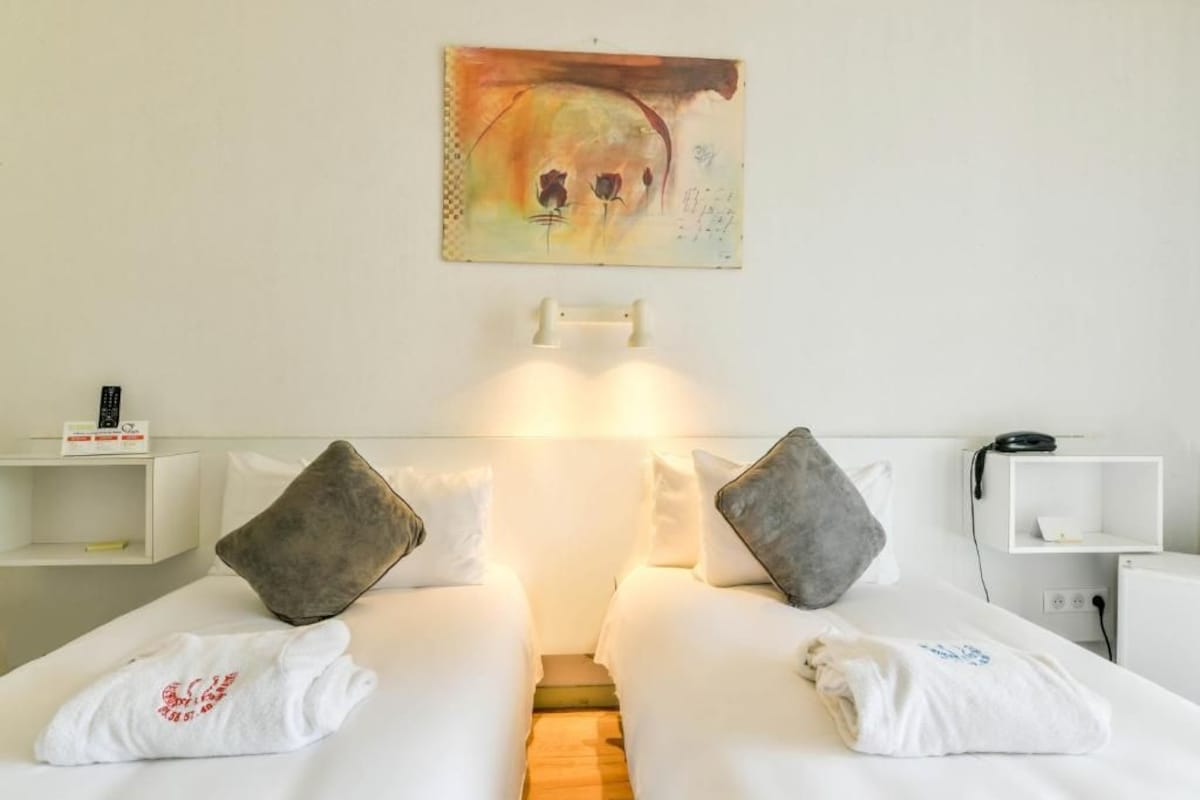 A hotel room with two beds, a painting on the wall, and a bedside table with a lamp.