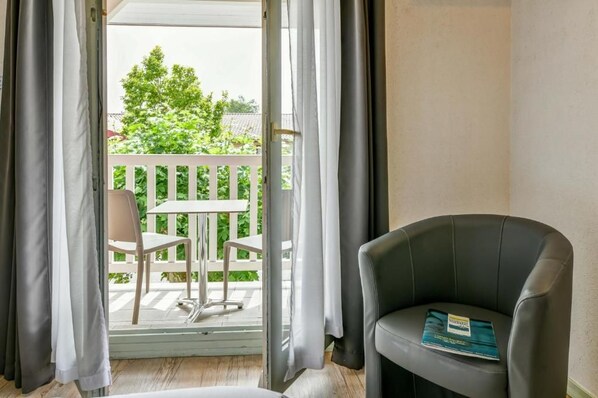 A room with a balcony, a chair, a table, and a book on the chair. - Logis Hotel Thermal (Saubusse)