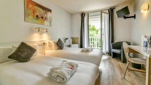 A hotel room with two beds, a desk, a chair, a TV, and a balcony with curtains. - Logis Hotel Thermal (Saubusse)
