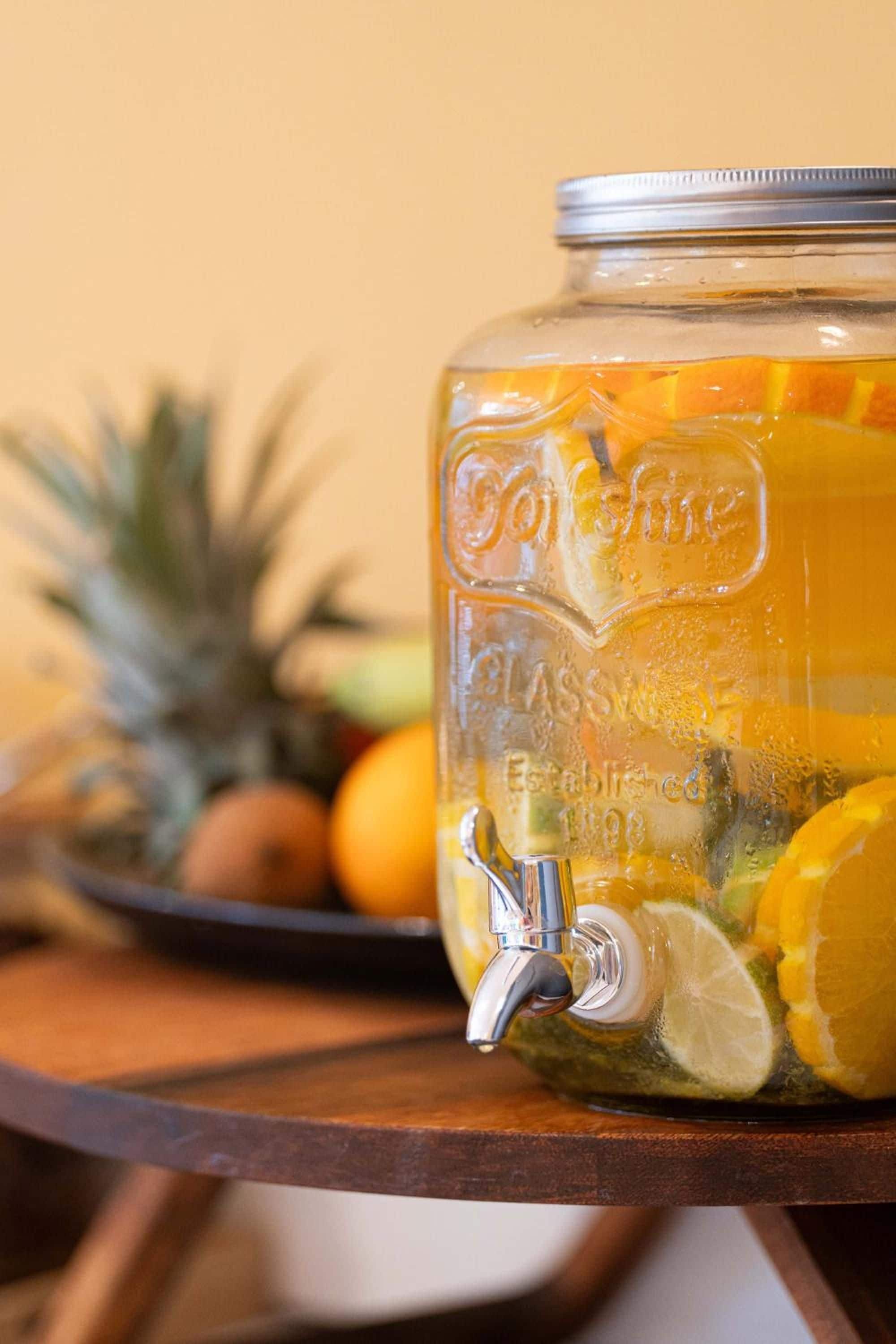 A glass jar with a tap, filled with a beverage and citrus slices, on a wooden table.