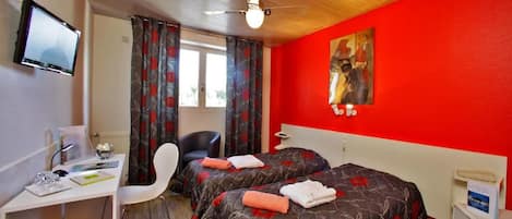 Une chambre d’hôtel avec deux lits, un bureau, une chaise, une télévision et un mur rouge.