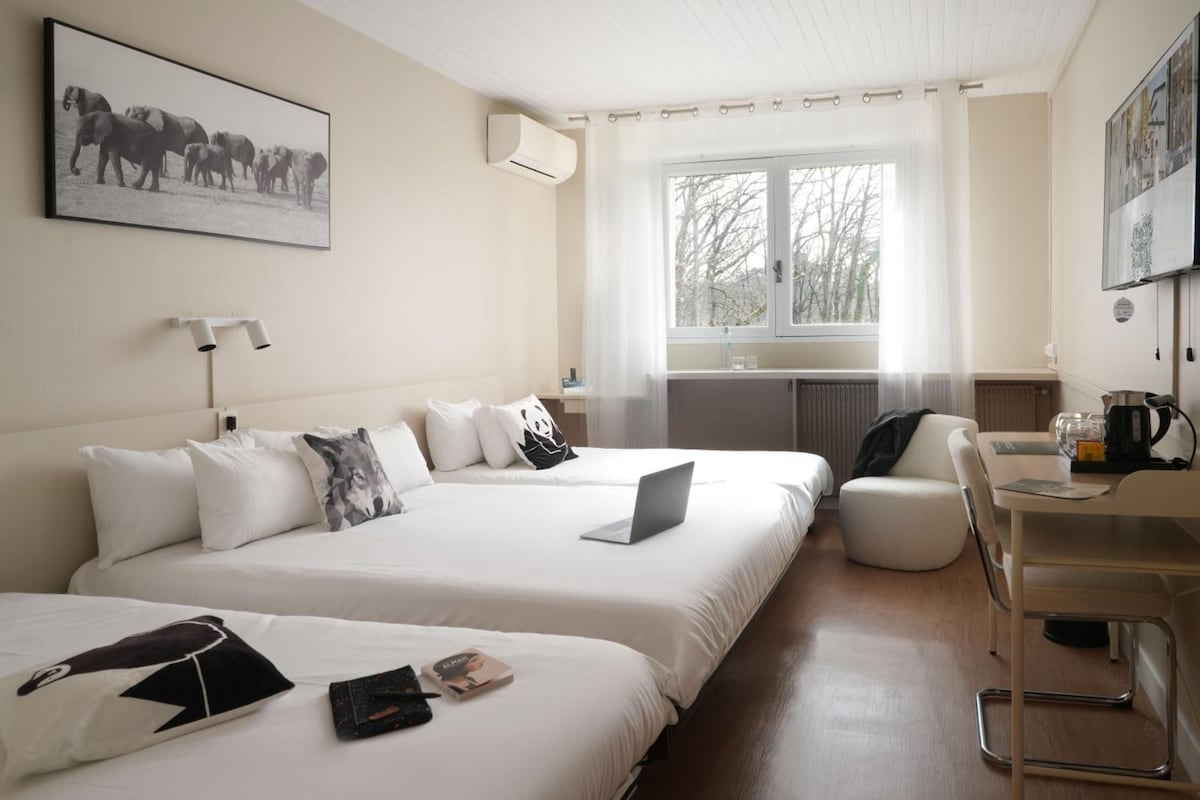 A hotel room with two beds, a desk, a chair, a window, and a radiator.