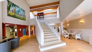 A spacious lobby with a central staircase, a dining area with wicker furniture, and a painting on the wall. - Logis Hotel Thermal (Saubusse)