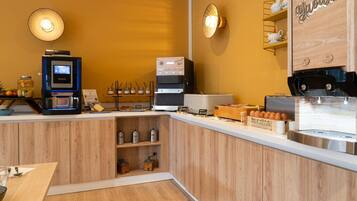 Interior de una cafetería con una máquina de café, una vitrina de pasteles y una barra de madera.
