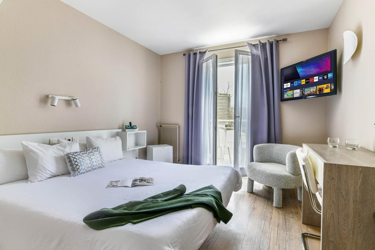 A hotel room with a bed, a desk, a chair, a TV, and a window with curtains.