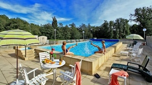 A swimming pool area with lounge chairs, umbrellas, and a table with fruits and drinks. - Logis Hotel Thermal (Saubusse)