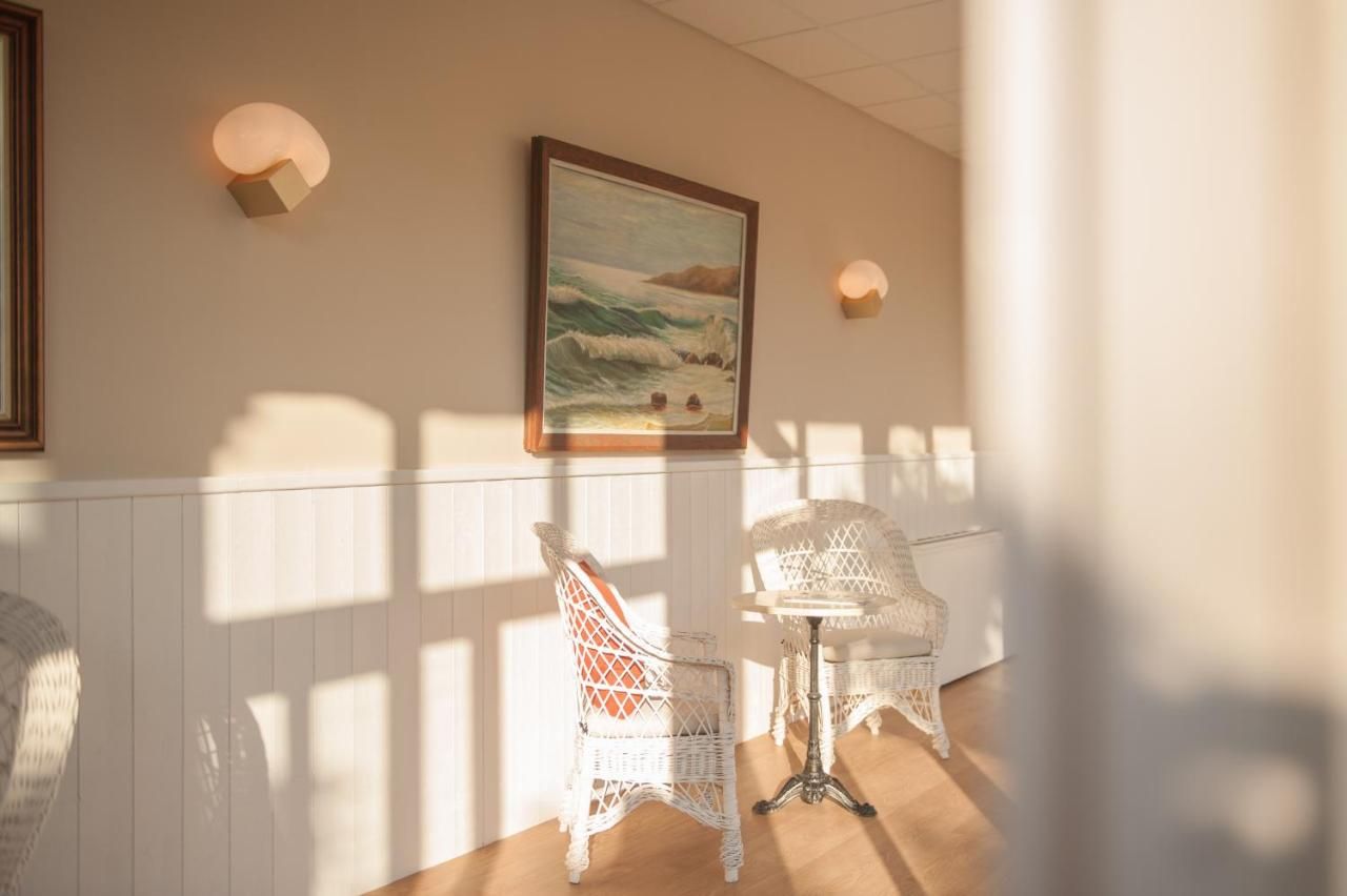 Una habitación con muebles de mimbre blanco, un cuadro enmarcado de una playa y luces fijadas a la pared.