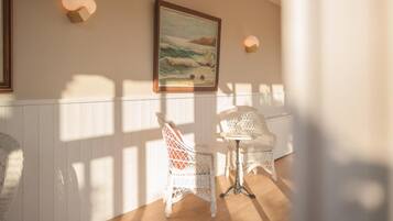 Una habitación con muebles de mimbre blanco, un cuadro enmarcado de una playa y luces fijadas a la pared.