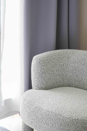 A corner of a room with a grey upholstered chair and a window with sheer curtains. - Logis Hotel Thermal (Saubusse)