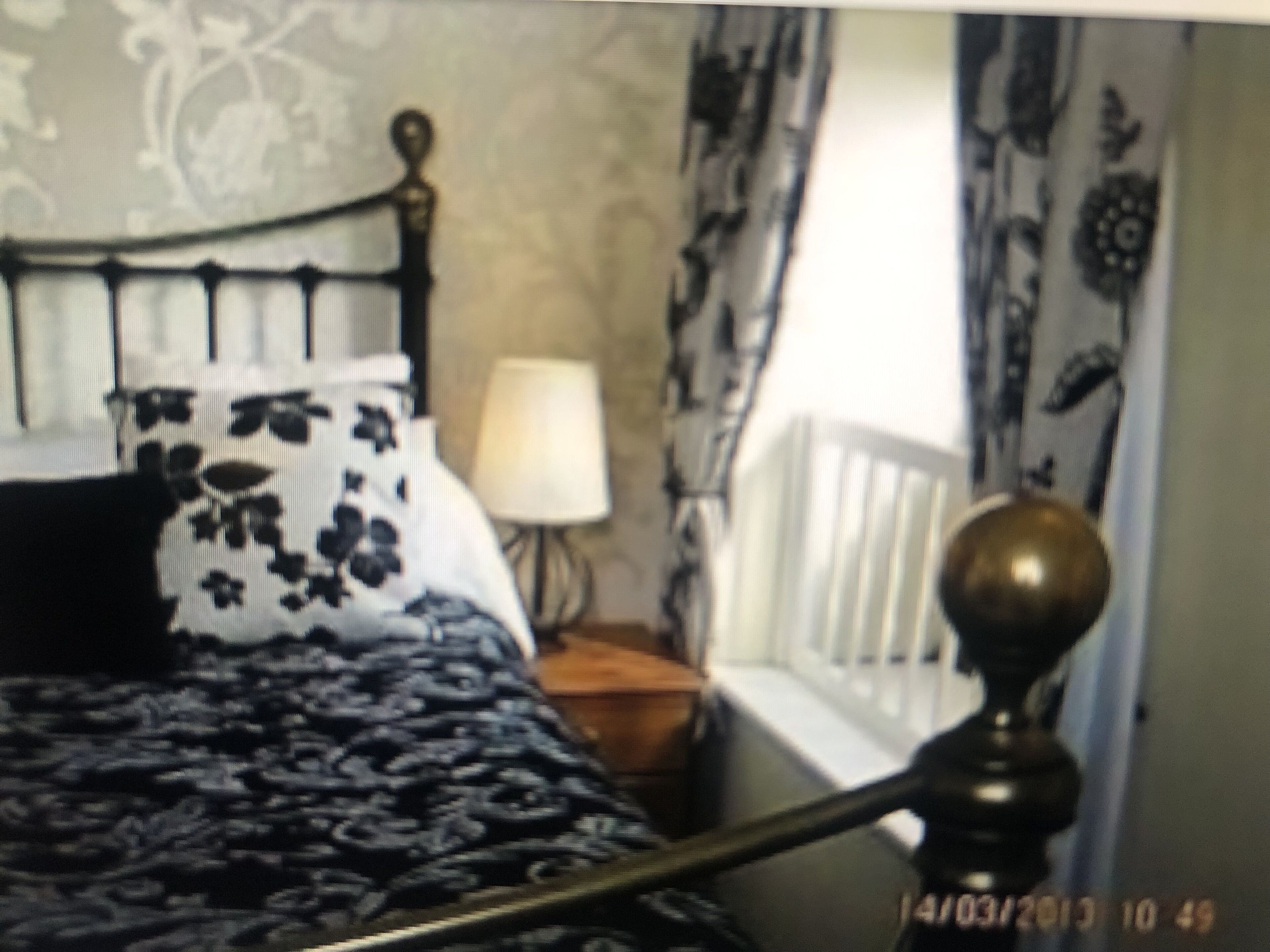 Un lit recouvert d’une couvre-lit à motifs floraux, une lampe de chevet et une fenêtre avec des rideaux.