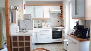 Una cocina compacta con armarios blancos, horno integrado y cafetera.