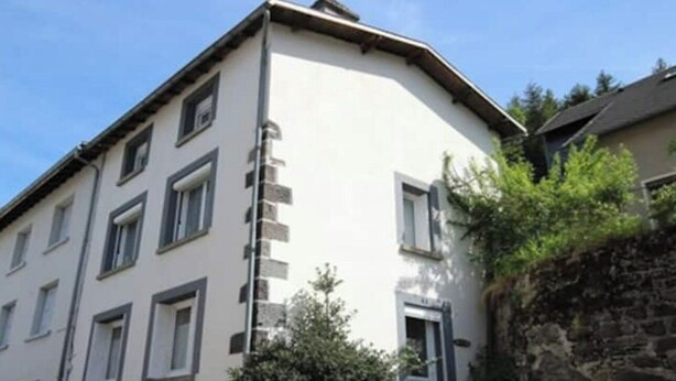 Un edificio de varios pisos con base de piedra y sección superior blanca, y una puerta con un pequeño ventanal.