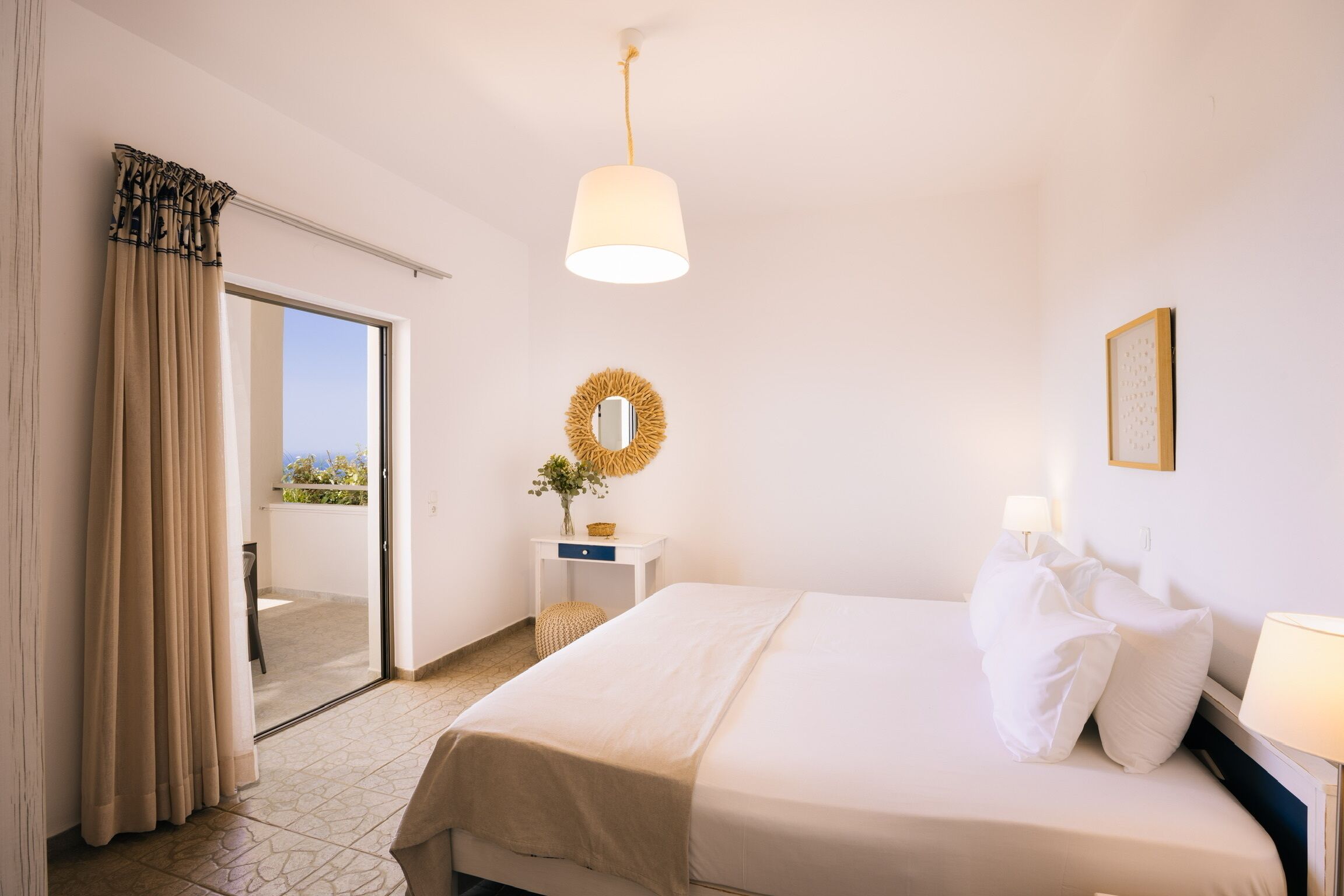 A hotel room with a bed, a nightstand, a lamp, a mirror, and a view of the outdoors.