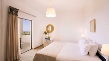 A hotel room with a bed, a nightstand, a lamp, a mirror, and a view of the outdoors.