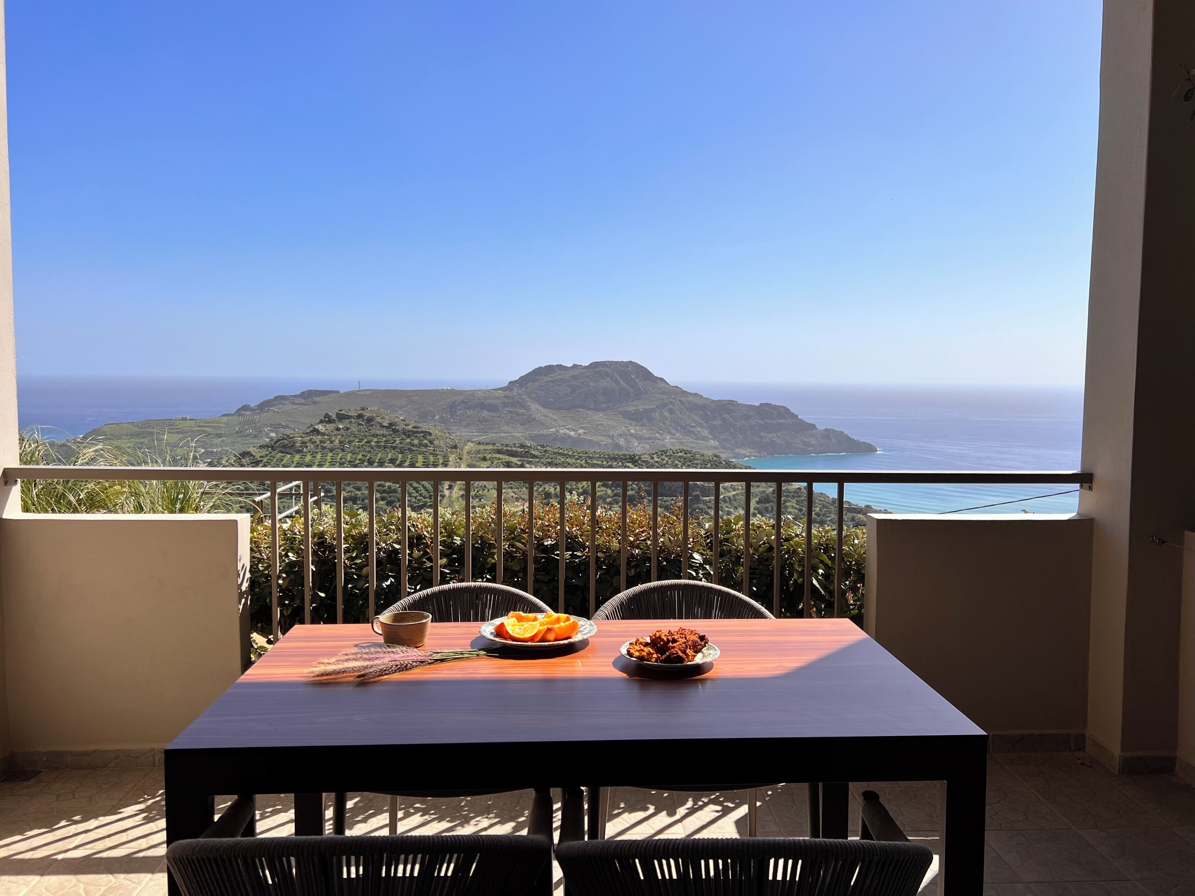 Een balkon met een tafel voor twee, met uitzicht op een kustlandschap en een berg in de verte.