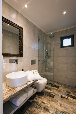 A modern bathroom with a large mirror, a round sink, a toilet, and a glass-enclosed shower area. - Villa Stella Suites (Agios Vasileios)