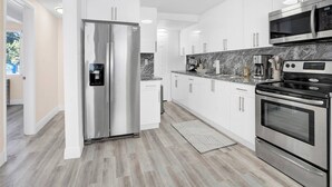 A modern kitchen with stainless steel appliances, white cabinetry, and a marble backsplash. - Villa Bonita | 6BR | Pool + Hot Tub (Miami)