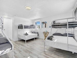 Een slaapkamer met stapelbedden, witte muren, een houten vloer en een klein tafeltje met een lamp.