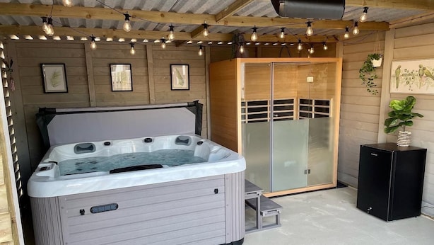 Un jacuzzi con revestimiento de madera, una puerta de cristal y una mesita auxiliar a un lado.