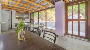 Un comedor rústico con mesas y sillas de madera, un ventanal con vistas al exterior y una botella de licor sobre la mesa.