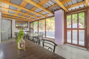 Un comedor rústico con mesas y sillas de madera, un ventanal con vistas al exterior y una botella de licor sobre la mesa.