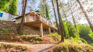 Una cabaña con pared de piedra y terraza de madera, rodeada de árboles.