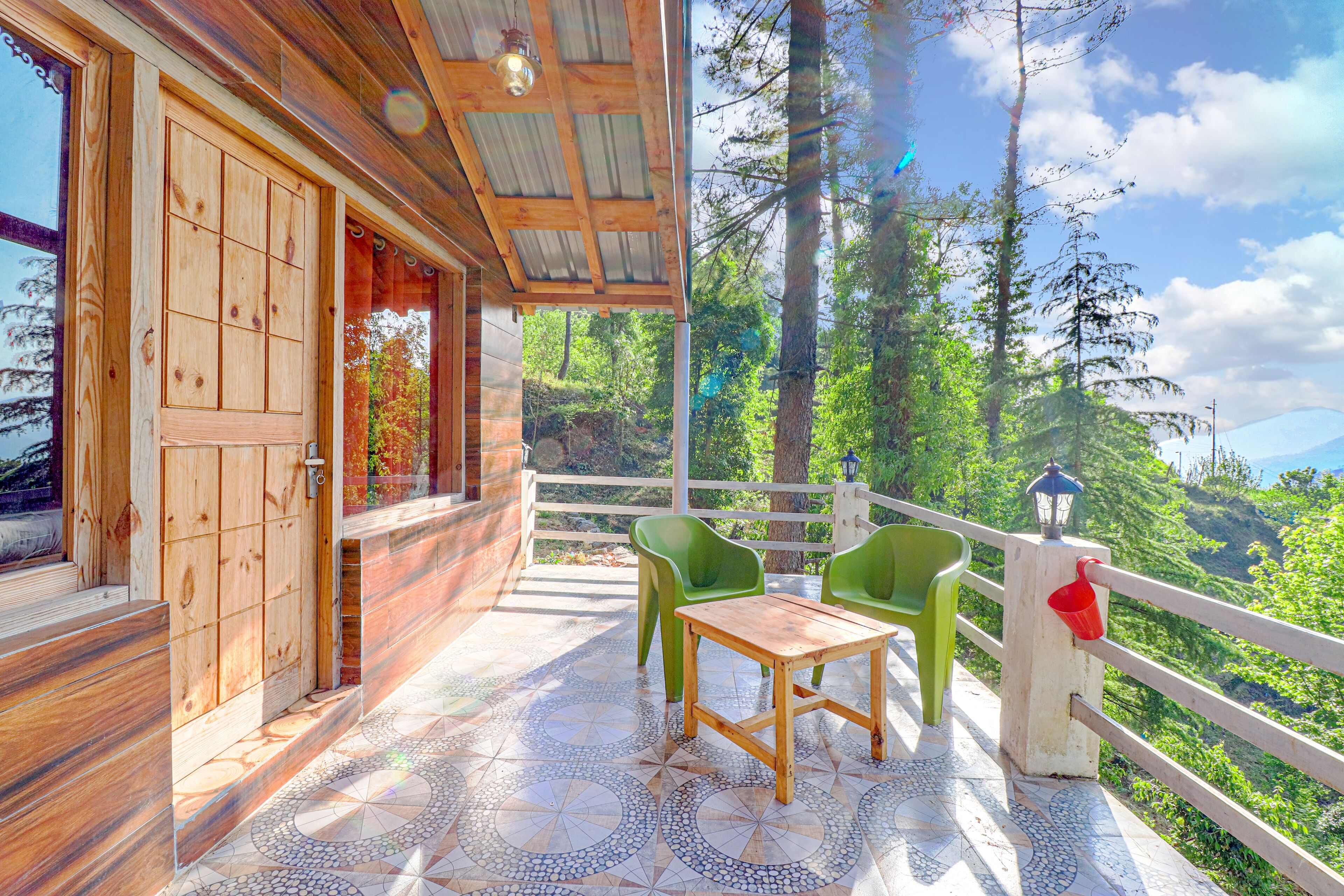 Eine Holzhütte mit gefliestem Patio, zwei grünen Stühlen und einem Tisch.