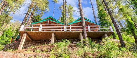 A wooden cabin with a green roof, situated on a hillside surrounded by trees.