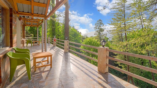 Un espacio al aire libre techado con una mesa y sillas de madera, una barandilla y vistas a un paisaje boscoso.