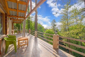 A covered outdoor area with a wooden table and chairs, a railing, and a view of a forested landscape. - Oak N Pine by Dumnu Homes (Kosiyakutoli)